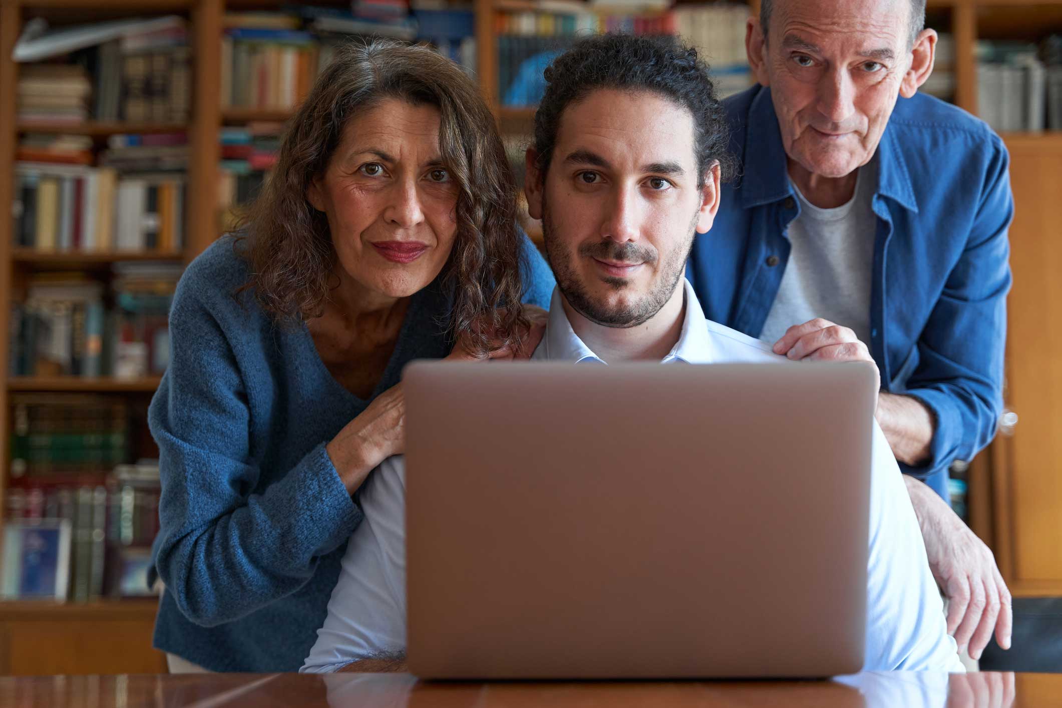 A mother, son, and father at a desk with a laptop staring intently.